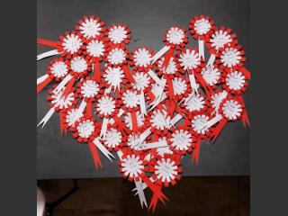 Biało - czerwone kotyliony, wykonane przez dzieci ułożone w kształt serca.