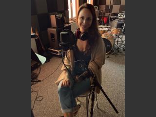 Maja Tabaka siedzi na krześle w studiu nagrań, przed nią mikrofon.