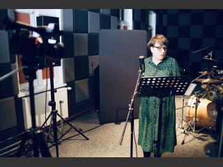 Kamila Guzewicz w studiu nagrań na Polanie Kultury. Przed nią pulpit i mikrofon, za nią perkusja.