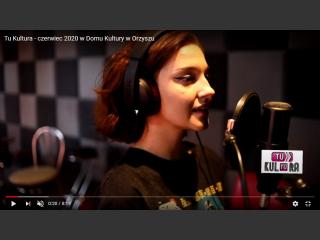 Zrzut ekranu z filmu na YouTube. W studiu nagrań, dziewczyna śpiewa, przed nią mikrofon.