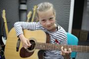 W studiu nagrań dziewczynka gra na gitarze.