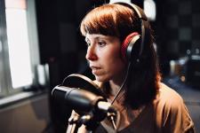W studiu nagrań kobieta, przed nią mikrofon.