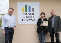Mężczyzna, Katarzyna Galczak i Jacek Foszczyński między nimi logo Polskiego Radia Orzysz. Kobieta trzyma książkę.