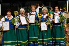 Kobiety z zespołu Orzyszanki w strojach ludowych trzymają w rękach ramki z dyplomami oraz słoneczniki. Podczas dożynek gminnych w Rostkach Skomackich.