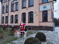Przed Pałacem Kultury święty Mikołaj z reniferami. Polana przystrojona w lampki, krzewy w czapkach z nosami i brodami.