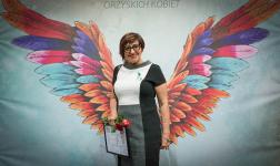 Anna Rogińska z różą i dyplomem na tle kolorowych skrzydeł.