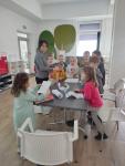 Grupa dzieci zgromadzonych przy stole, przeglądających kartki z zadaniami i książki