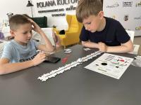 Dwóch chłopców przy stole, na stole puzzle do kodowania. Za nimi na ścianie napis Polana Kultury.