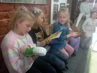 3 dziewczynki z zespołu Orzyszanki OD NOVA oglądają nagrody i dyplomy Orzyszanek, w tle siedzą dziewczynki.
