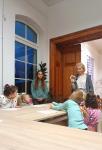 Pani Bożena Stankiewicz stoi przed dziećmi z tabliczką ze zwierzątkiem. Dzieci siedzą przy stole.