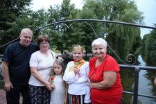 5 osób, trójka doroslych, oraz dwie dziewczynki pozują do zdjęcia na Moście Zakochanych w Orzyszu. Za nimi rzeźba gołąbków.