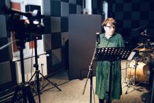Kamila Guzewicz w studiu nagrań na Polanie Kultury. Przed nią pulpit i mikrofon, za nią perkusja.