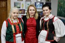 Dwie kobiety z strojach ludowych, między nimi Pani Dyrektor Polany Kultury w Orzyszu. Za nimi na ścianie obrazy, wycinanki. 
