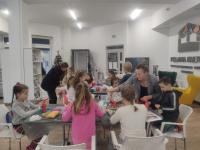 Dzieci siedzą przy stołach i tworzą ozdoby świąteczne