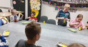 Dzieci siedzą przy stole i malują na żółto rolki.