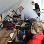 Młodzież w studiu Radia Orzysz. Przed nimi biurka z monitorami i statywy mikrofonowe 