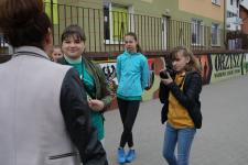 Młode dziewczyny przeprowadzają wywiad w mieszkanką Orzysza na ulicach miasta Orzysz. Jedna z dziwczyn z prawej strony trzyma aprat i robi zdjecia 