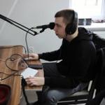 Chłopak w studiu Radia Orzysz. Przed nim biurko i statyw mikrofonowy 