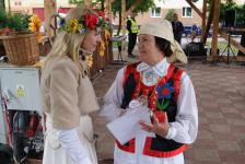 Przy scenie Pani Dyrektor Polany Kultury rozmawia z kobietą w stroju ludowym. Kobieta trzyma w reku dyplom i drewnianego kwiatka.