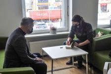 Dwóch mężczyzn na fotelech przy stoliku. Z prawej strony Artur Olchowy podpisuje książkę. W bibliotece Polany Kultury.