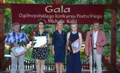 Pięć osób na scenie. Trzy osoby trzymają ramki z dyplomami i róże. Po prawej stronie Zbiegniew Włodkowski Burmistrz Orzysza.