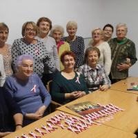 Kobiety z Klubu Seniora w Orzyszu. Przed nimi na stole biało czerwone wstązki i Orzełkiem. 