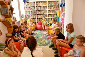 Dzieci w kąciuku dziecięcym w bibliotece. Przy ścianach regały z książkami.