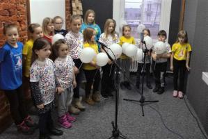Dzieci z zespołu Neonutki w studiu nagrań. Część dzieci w pierwszym rzędzie trzyma balony. Przed nimi statywy mikrofonowe.
